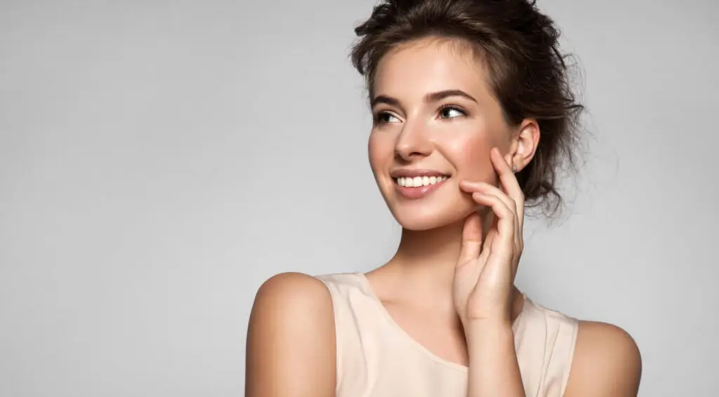 Femme souriante touchant son visage, fond gris clair